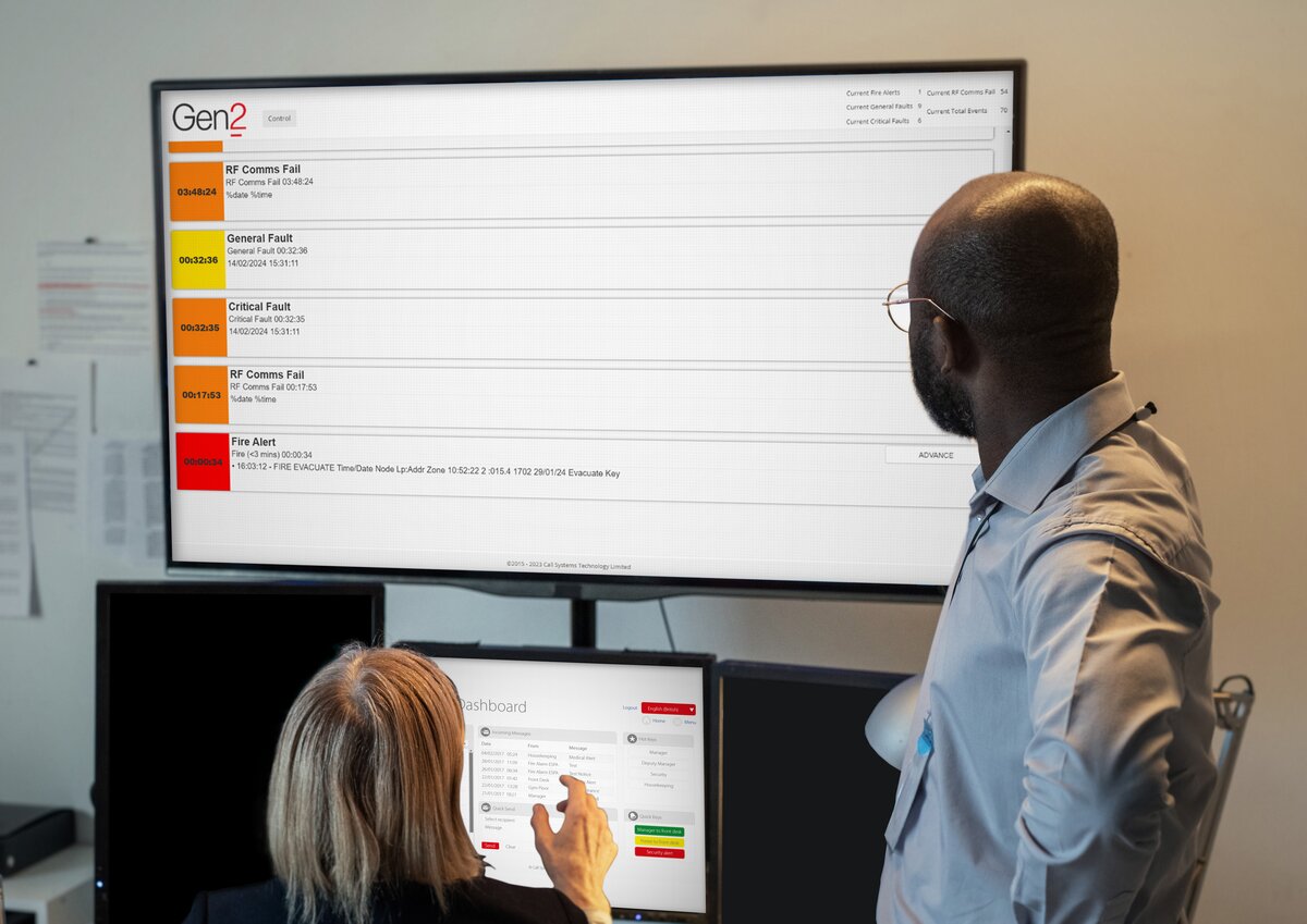 A man looking at a screen displaying Gen2 software and talking to a lady who is also looking at a screen displaying Gen2 software