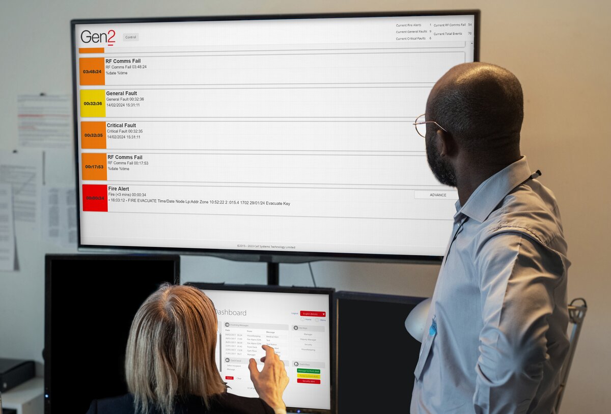 A man looking at a screen displaying Gen2 software and talking to a lady who is also looking at a screen displaying Gen2 software