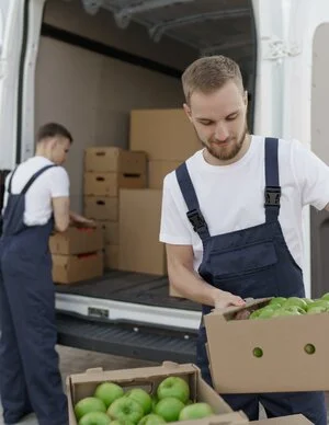 Two men wearing dungarees whilst delivering crates of apples